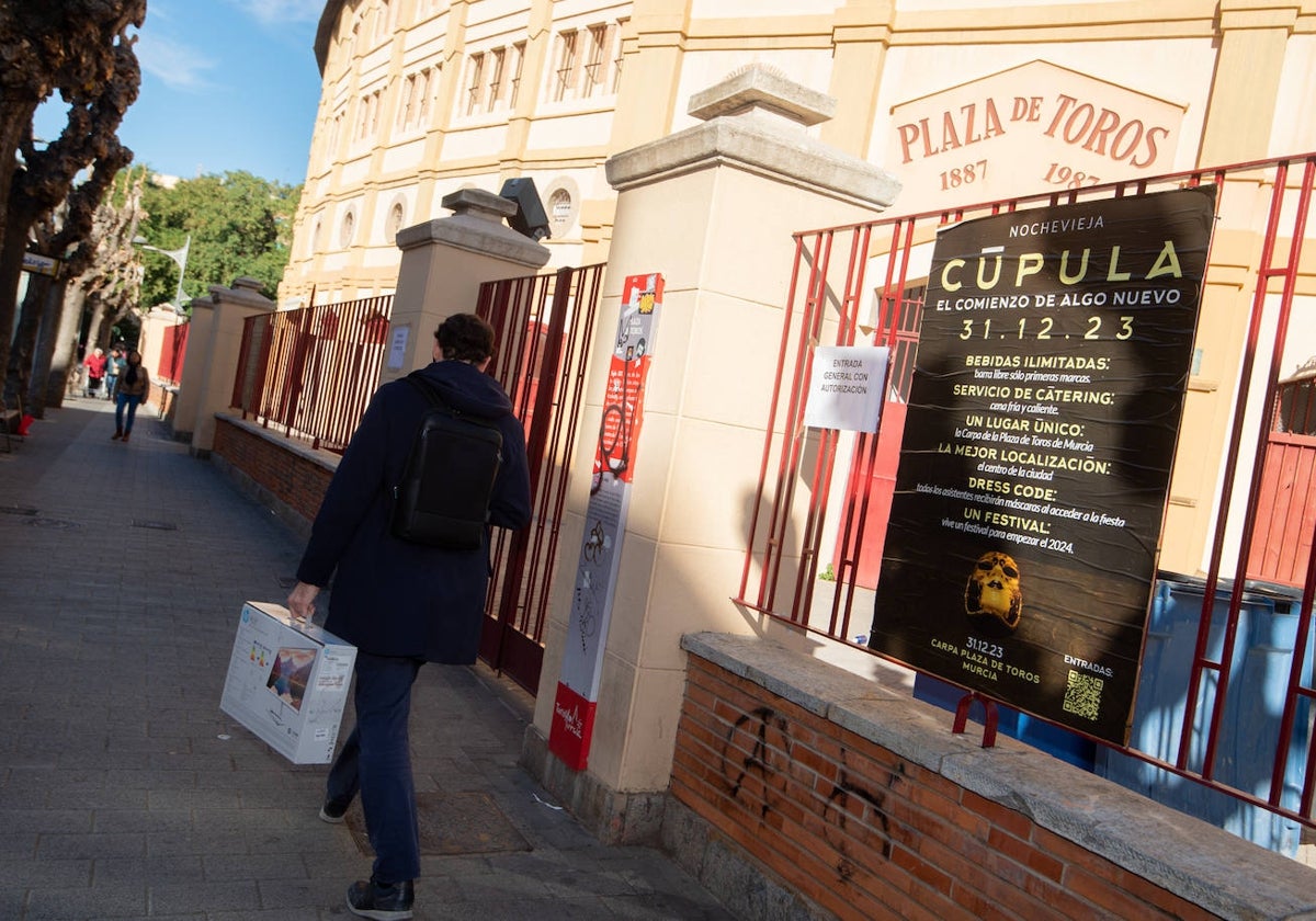 Un viandante pasa junto al cartel de la macrofiesta anunciada en la Plaza de Toros de Murcia.