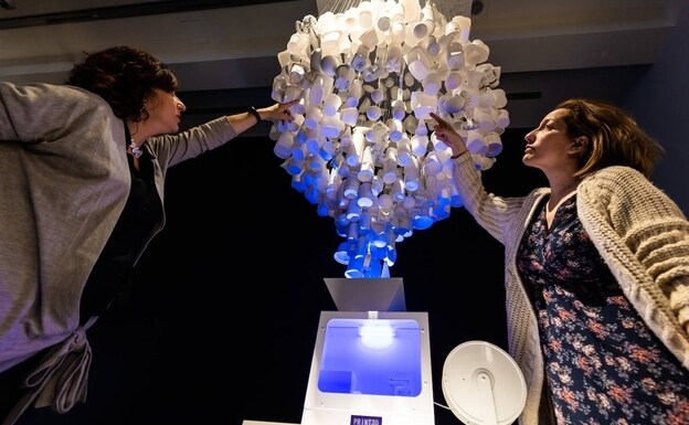 Two women touch a shredder for recycling in the exhibition 'PRINT3D.  Reprint reality' by CaixaForum Madrid.