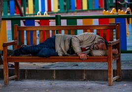 Una persona sin hogar descansa en un banco de un parque de Murcia.
