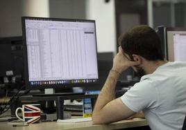 Un trabajador mira con actitud cansada una pantalla de ordenador en una oficina.