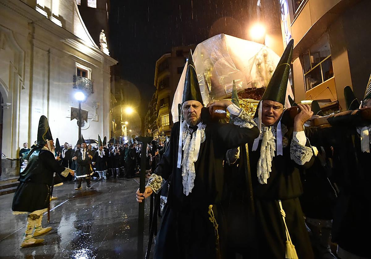 Semblantes serios de los puntas de vara de uno de los pasos de La Esperanza, cubierto de plásticos, ante la iglesia de San Pedro en pleno aguacero.