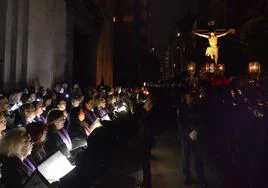 Una coral entona una pieza religiosa al paso del Cristo del Refugio en su procesión por la ciudad a oscuras.