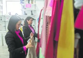 Las dependientas actuales de Moda Re-, Mari Carmen y Carina, colocan la ropa en los percheros de la tienda.