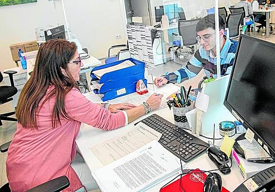Una funcionaria atiende a un vecino en Torre Pacheco de forma manual, mientras el ordenador de su mesa permanece apagado.