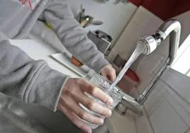 Una mujer llena un vaso de agua del grifo.