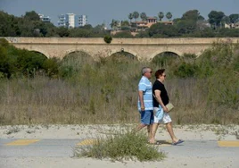 Dos vecinos caminan sobre los restos de la antigua carretera. Al fondo, el puente de Campoamor sobre la desembocadura del río Nacimiento.