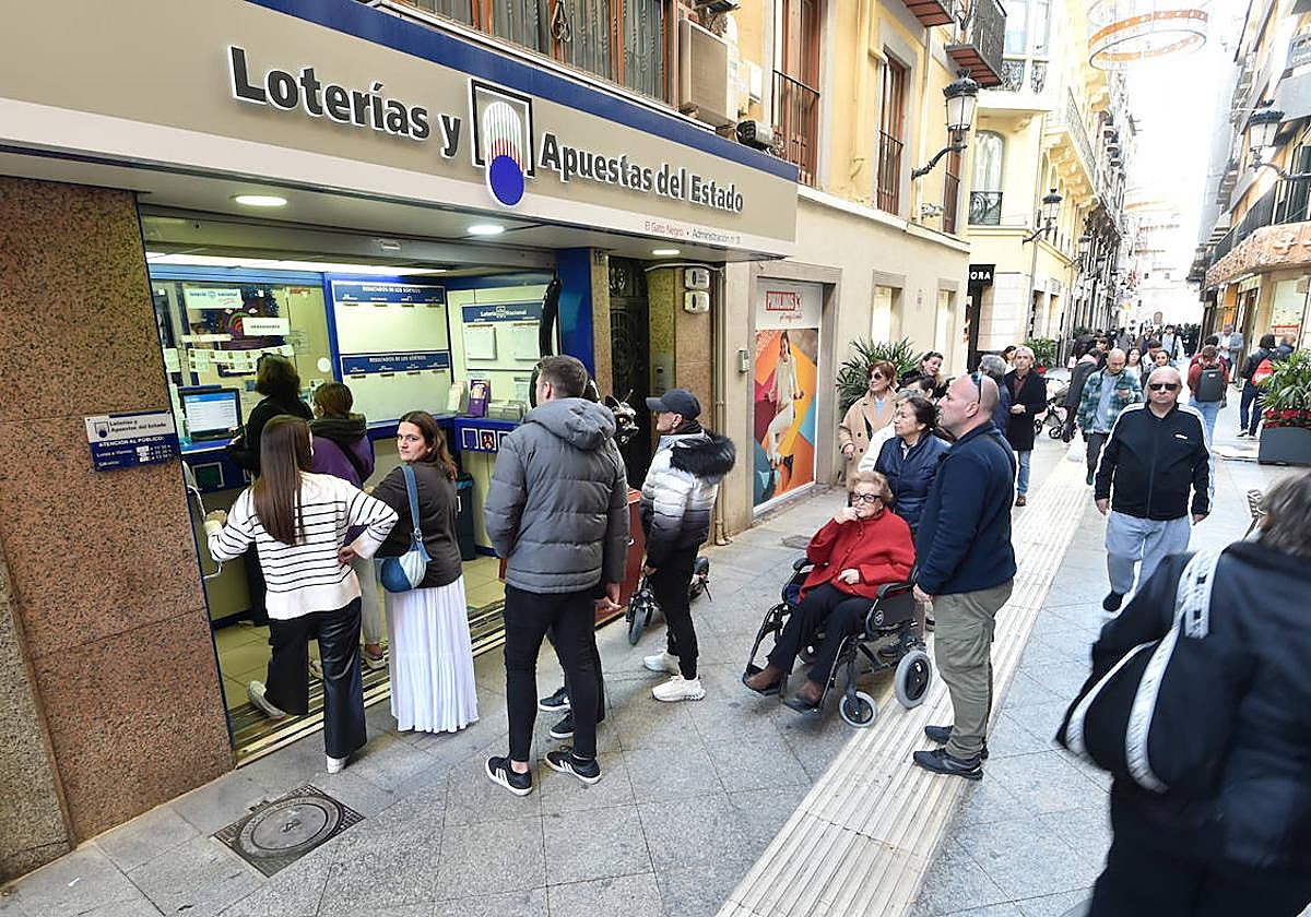 Unos ciudadanos esperan su turno para comprar un décimo de Lotería de Navidad de la administración de El Gato Negro en Murcia