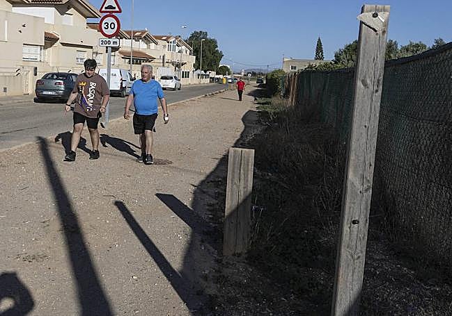 Dos vecinos pasan junto a dos postes con los carteles rotos.