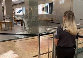 Una guardia de seguridad del centro comercial observa el agujero que los atracadores han hecho en el cristal de la tienda.