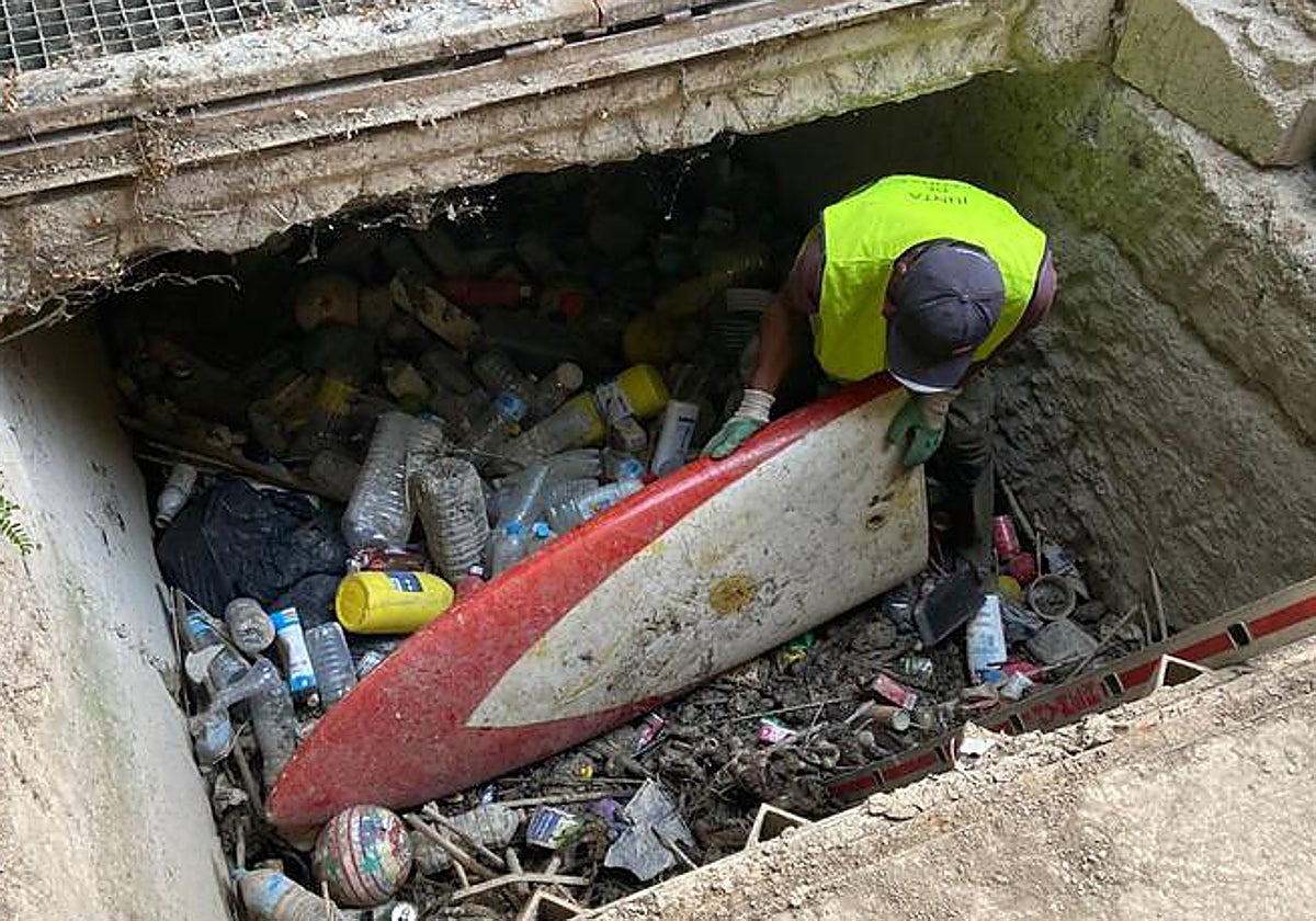Un operario saca una tabla de surf durante la limpieza de la acequia de Barreras, en Barriomar.
