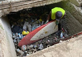 Un operario saca una tabla de surf durante la limpieza de la acequia de Barreras, en Barriomar.
