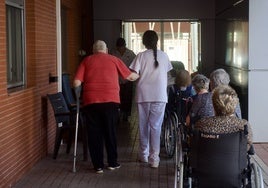 Una anciana se apoya en una trabajadora para caminar en una residencia de personas mayores en Murcia.