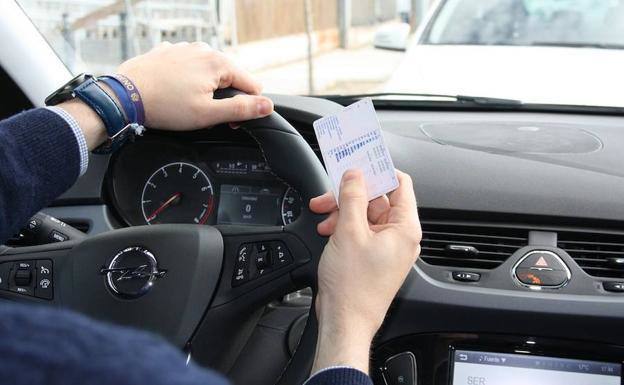 Una persona al volante con el carné de conducir en la mano.