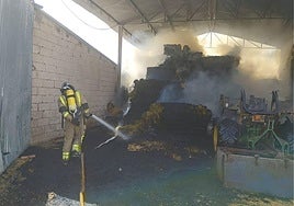 Un efectivo de bomberos sofoca las llamas en las balas de paja almacenadas.