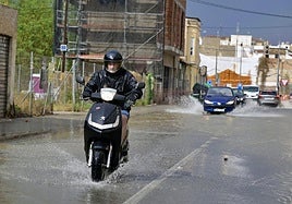 Un motorista cruza por una calle con acumulación de agua durante un episodio de tormentas.