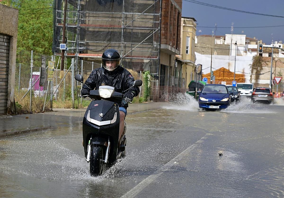 Un motorista cruza por una calle con acumulación de agua durante un episodio de tormentas.