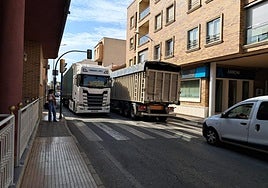 Una mujer, con un bebé en brazos, espera para cruzar un paso de peatones en la avenida Poeta Julián Andúgar, en Santomera, junto a dos camiones.