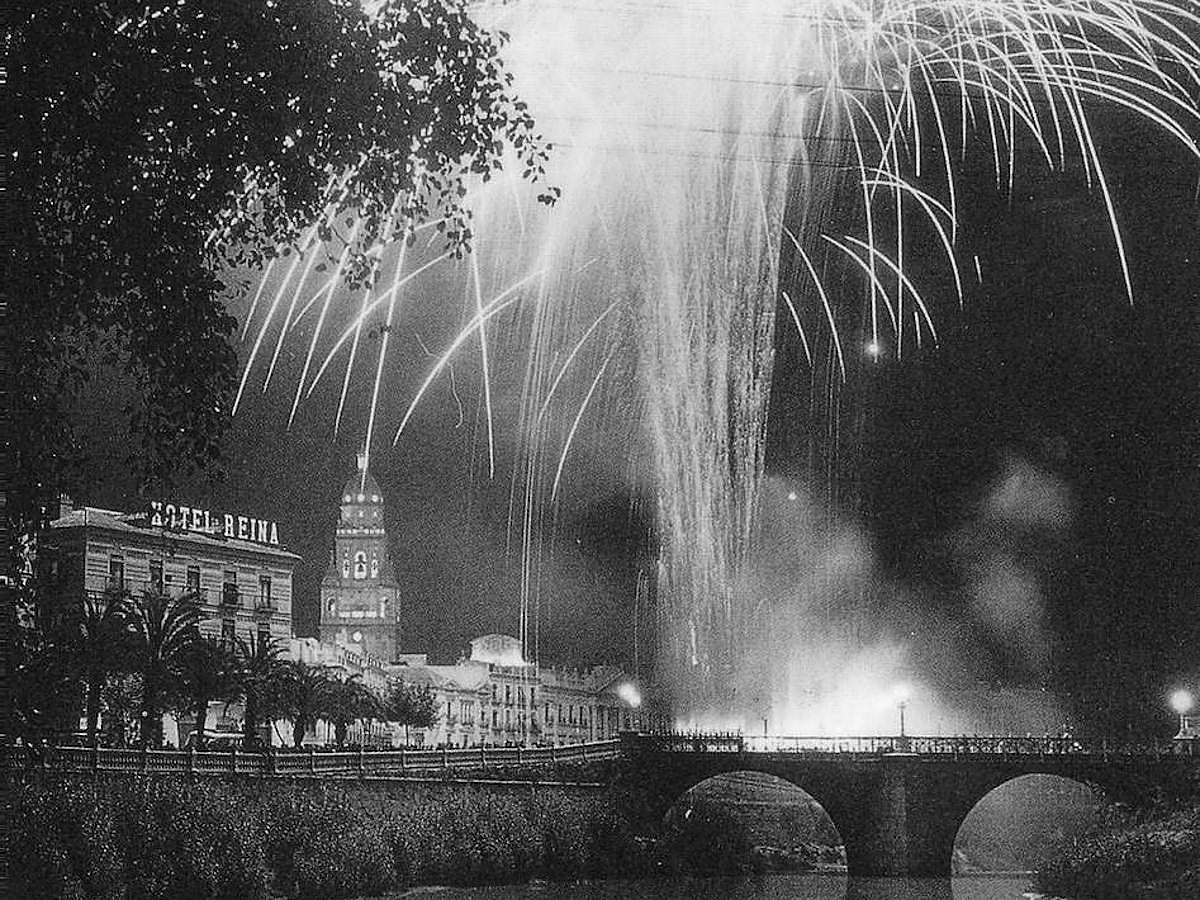 Una de las más bellas fotografías de un castillo de fuegos artificiales sobre el río Segura y, a la derecha, el histórico hotel Reina Victoria. En el centro, la torre de la catedral iluminada.