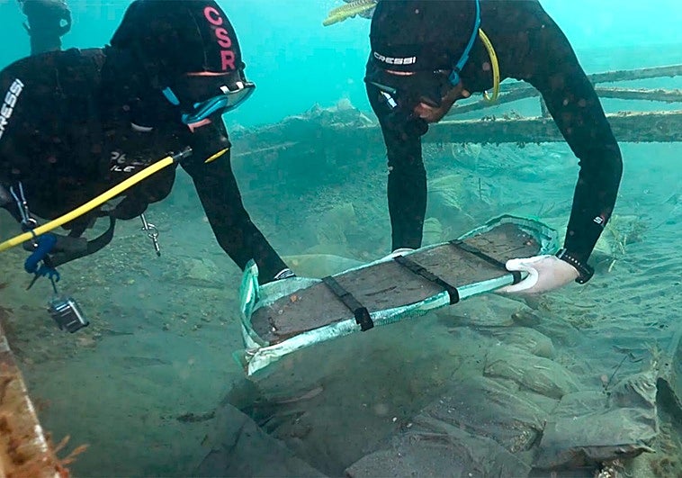 Dos arqueólogos trasladan a la superficie el primer fragmento dle barco fenicio de Mazarrón.