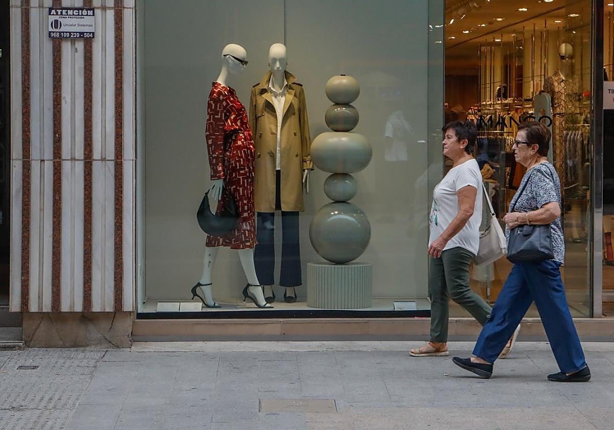 Dos mujeres en manga corta, junto a un escaparate con ropa de la temporada otoño-invierno.