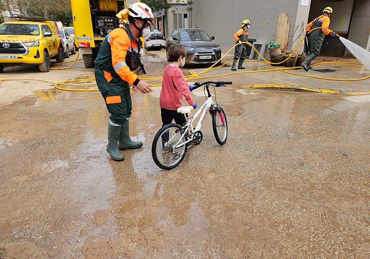 Un brigada forestal del dispositivo de la Comunidad, con un niño en bicicleta en Paiporta.