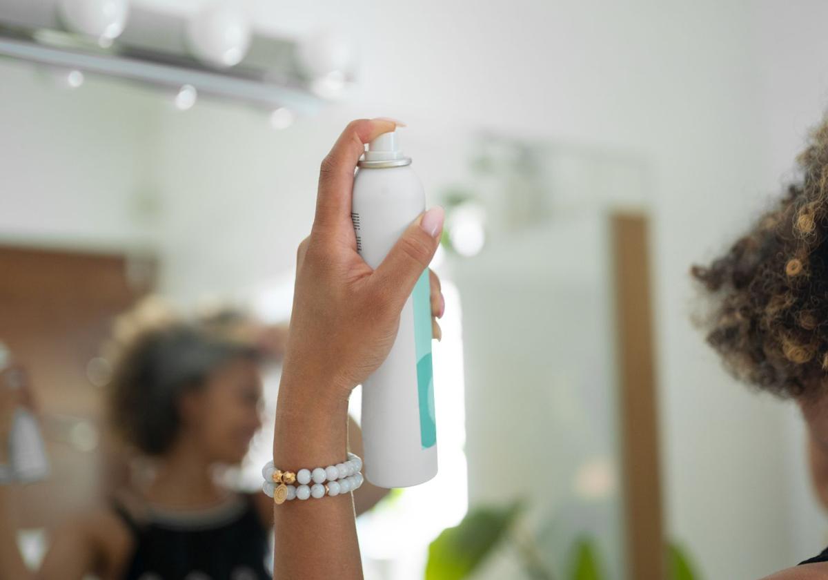 Una chica aplicando en su cabello champú en seco..