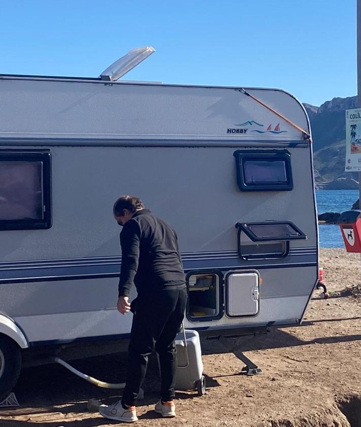 Imagen secundaria 2 - Autocaravanas instaladas al borde de la playa del Arroz y en sus inmediaciones, con elementos desplegados como sillas y tumbonas. El propietario de una autocaravana transporta un depósito del váter químico que acaba de vaciar junto al cartel de la playa del Arroz, que prohíbe expresamente acampar y aparcar.