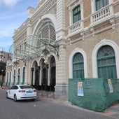 Un taxi aparcado frente a la puerta principal de la estación de trenes, donde también hay una malla verde que esconde un contenedor de obra.