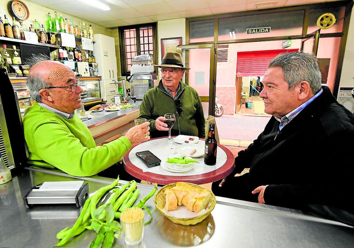 Imagen principal - Arriba: Tres clientes habituales despachan unas habas y una tapa de morcón yeyé, la semana pasada. Abajo: Luis Miguel Galindo, de niño, junto a su tío Manuel y la máquina de hacer sifón en la pared, a finales de los años 60. Luis Miguel Galindo, en la actualidad, sirve un vermú con sifón tras la barra.