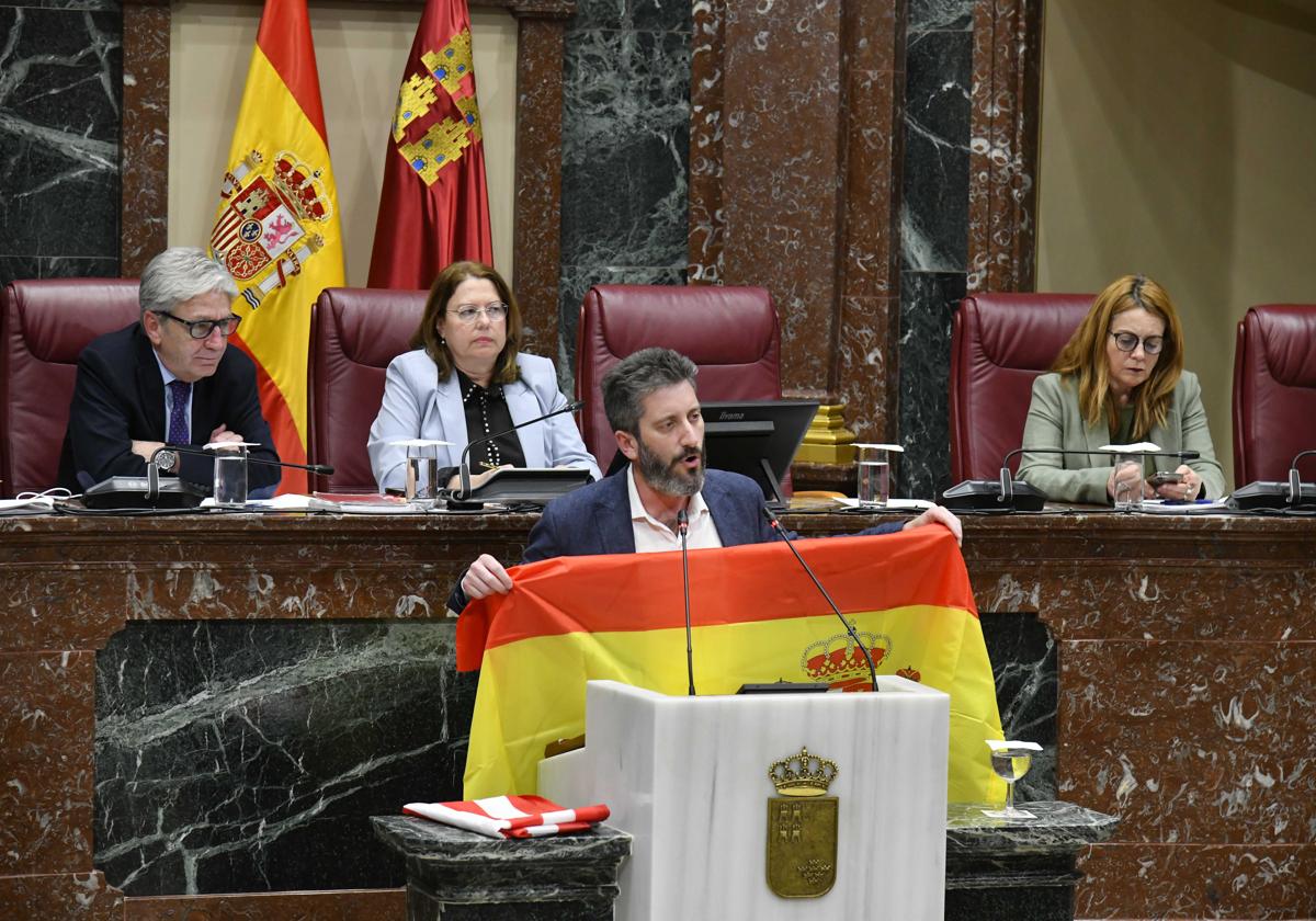 Víctor Egío sostiene la bandera de España, este martes, durante su intervención en la Asamblea Regional.