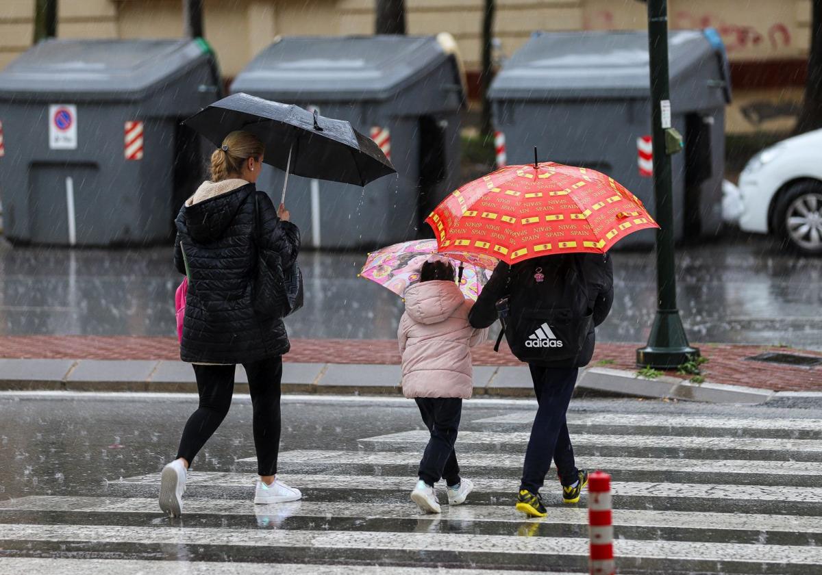 Una madre acompaña a sus hijos en un día de lluvia en Murcia.