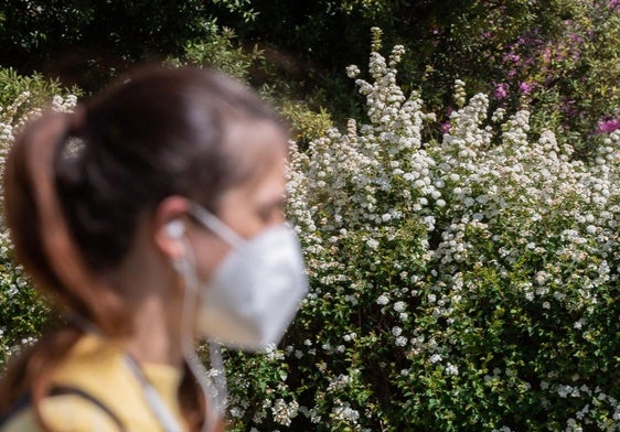 Una mujer pasea con mascarilla por un parque para evitar reacciones alérgicas.