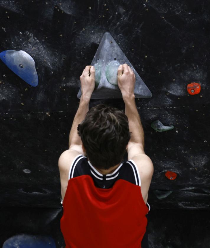 Imagen secundaria 2 - Aficionados a la escalada buscan la siguiente piedra donde sujetarse para no caer a las colchonetas que abrazan la pared. 