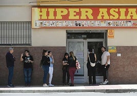 Una cola de ciudadanos esperan en la puerta de un bazar para hacer sus compras.