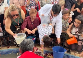 Vecinos con cubos de agua, mientras el cura, de espaldas, sujeta la cruz.