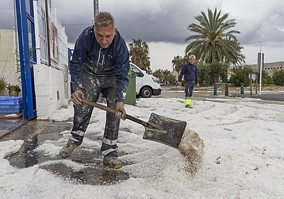 Un hombre retira el granizo de la puerta de su empresa este jueves en el polígono de Mula.