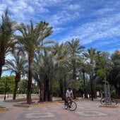 Dos ciclistas pasean por la plaza Constitución, junto a las palmeras y oliveras que cambiarán de lugar.