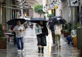 Viandantes con paraguas para protegerse de la lluvia en la calle Trapería de Murcia, este viernes.