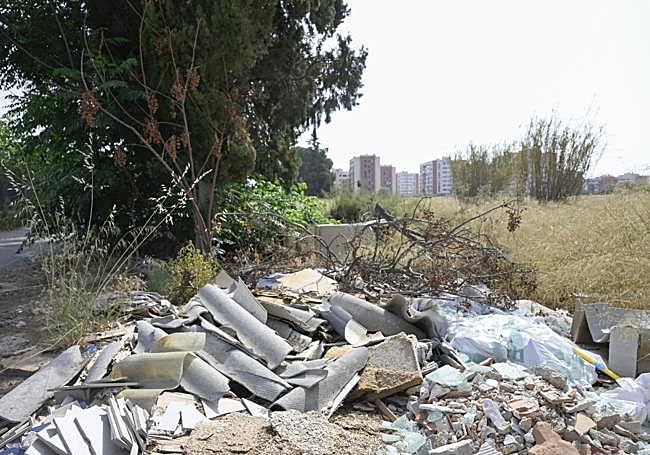Escombros en una senda próxima a las viviendas; al fondo aparecen varios bloques de pisos de la urbanización.
