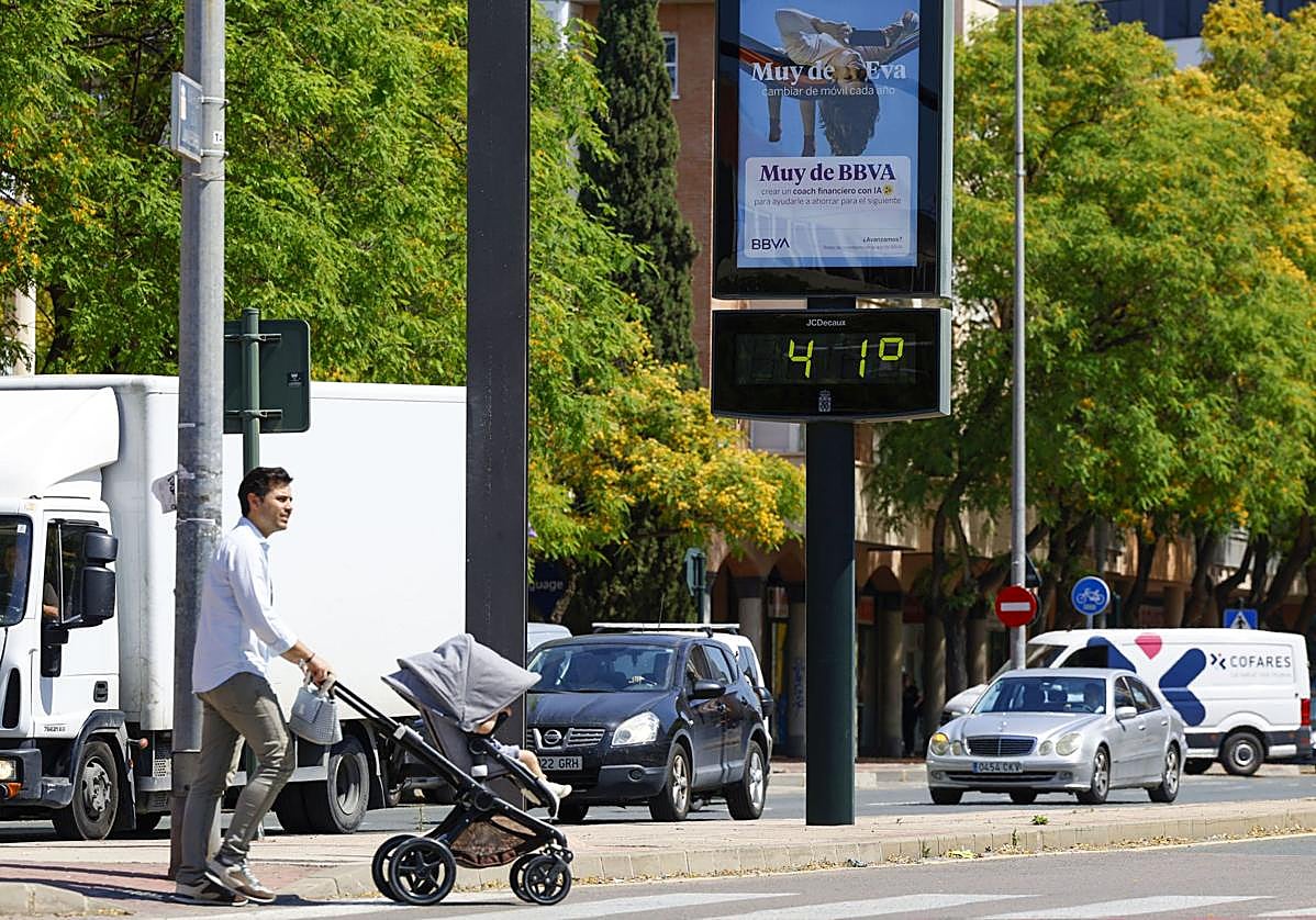Un hombre cruza un paso de peatones empujando un carrito de bebé, junto a un termómetro que marca 41 grados en Murcia.