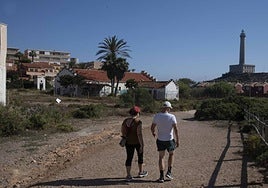 Una pareja camina a orillas del mar por el camino que pasa frente a la estación de telegrafía. Al fondo, el faro de Cabo de Palos.
