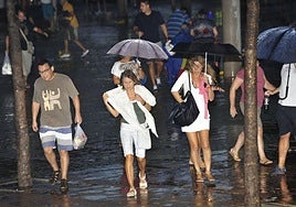 Vecinos de Murcia transitan bajo la lluvia durante una tormenta de verano.