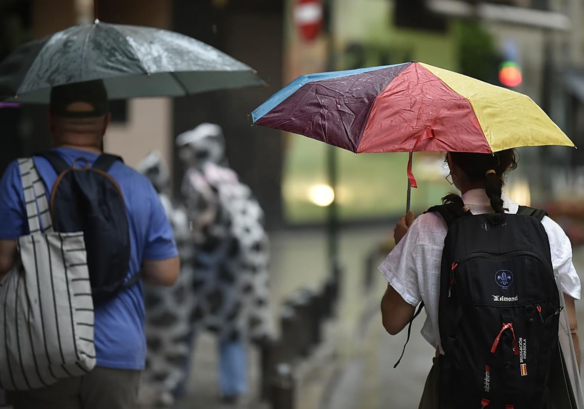 Peatones caminan por el centro de Murcia protegiéndose de la lluvia con paraguas.