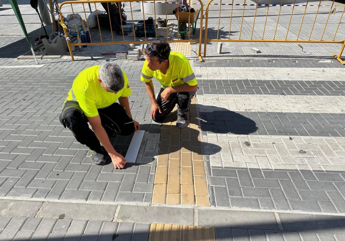Dos operarios toman medidas en uno de los pasos de peatones que tendrá el servicio.