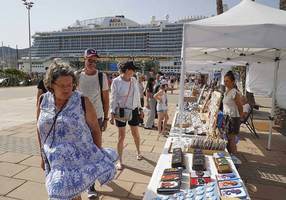 Turistas recién desembarcados pasan ante los puestos de artesanía instalados en el Muelle.