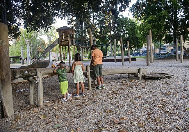 Tierra, árboles, agua. Unos niños juegan en el jardín de la Pólvora de Murcia con una canalización de agua, en un espacio marcado por el suelo de zahorra y las sombras que proyecta el arbolado.