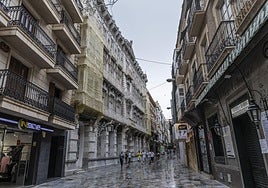 Cartageneros y turistas caminan frente a la fachada de la Casa Cervantes, con sus miradores tapados con mallas amarillas.