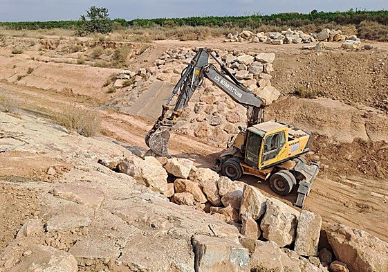 Una excavadora levanta una pared de escollera en el último tramo del cauce de la rambla.