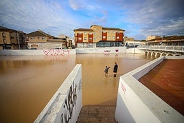Un hombre y un niño, con botas de agua, observan el caudal acumulado en el cauce de la rambla junto al polideportivo municipal de San Javier, uno de los municipios más afectados.