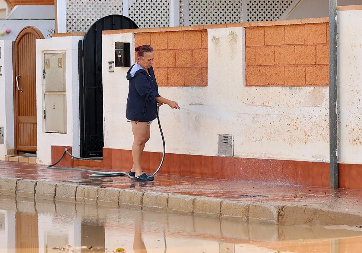 Una mujer limpia la calle, llena de barro tras las lluvias de la dana.
